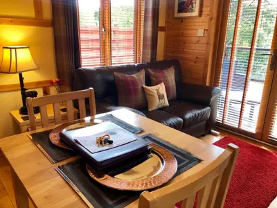 a living room with a table and a leather couch at Rashfield Sheilings - Quiet Riverside Lodges for Couples near Pucks Glen in Dunoon