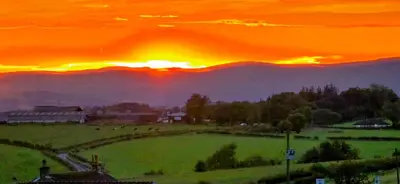 a sunset over a field with the sun setting behind mountains at The Green Monkey Lux Suite at The Grumpy Schnauzer B&B Private Hot Tub, Gym, Breakfast, Stunning! in New Monkland