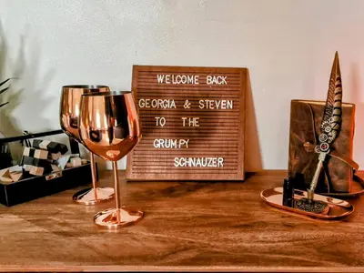 two wine glasses sitting on a table with a sign at The Green Monkey Lux Suite at The Grumpy Schnauzer B&B Private Hot Tub, Gym, Breakfast, Stunning! in New Monkland