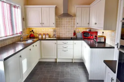 a kitchen with white cabinets and black counter tops at Osborne Cottage in Southend