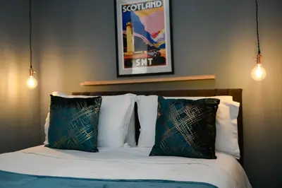 a bed with two pillows and a picture on the wall at The Gallery Apartment - Spacious, Town Centre, Walkable to Ferry Terminal, in Oban