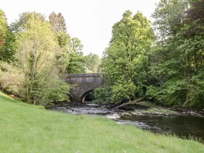 a river with a bridge in the middle of a field at Maisie's Cottage in Dunblane