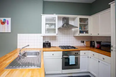 a kitchen with white cabinets and a sink at Modern, Light-filled and Sleek West End Apartment in Glasgow