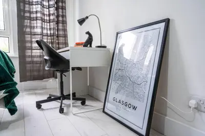 a desk with a sign and a chair and a picture at Cheerful 2 Bedroom Homely Apartment, Sleeps 4 Guest Comfy, 1x Double Bed, 2x Single Beds, Free Parking, Free WiFi, Suitable For Business, Leisure Guest, Contractors, QE Hospital, Glasgow, Near Airport & City Centre, Perfect For Common Wealth Games 2026 in Glasgow