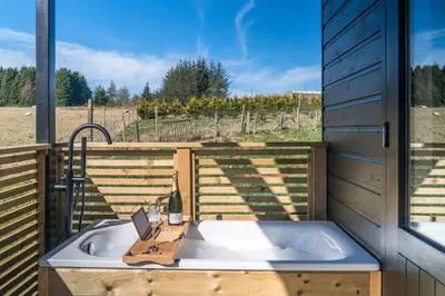 a bath tub with a bottle of wine and a bottle of wine at The Trossachs Collection in Kepculloch