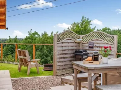 a patio with a grill and a table and a chair at Lochinvar - Clydesdale Log Cabin with Hot Tub in Airdrie