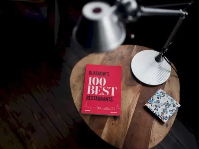 a red book sitting on a wooden table with a lamp at Beautiful, traditional 2 bed flat w free parking - Pass the Keys in Glasgow
