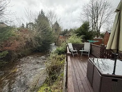 a wooden deck with two chairs and a table next to a river at Deer lodge in Auchterarder