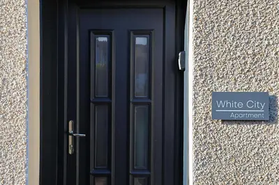 a black door with a sign in front of a building at The White City Apartment in Oban