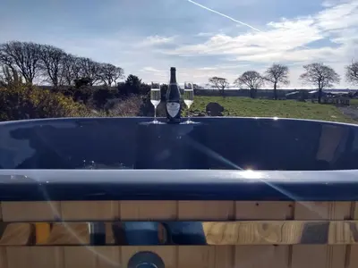 a blue bath tub with a bottle of wine in it at Cleeves Cabins Arran Luxury Lodge with hot tub in Dalry