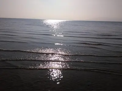 a beach with the sun reflecting on the water at Cleeves Cabins Arran Luxury Lodge with hot tub in Dalry