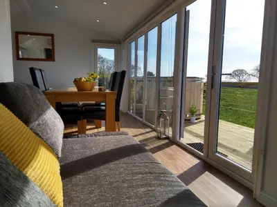 a living room with a dining table and sliding glass doors at Cleeves Cabins Arran Luxury Lodge with hot tub in Dalry