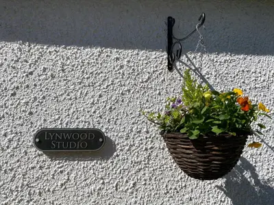 a basket of flowers hanging on a wall with a sign at Lynwood Studio in Oban