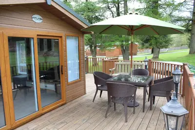 a deck with a table and chairs and an umbrella at Lazy Days Lodge, Glendevon, Perthshire in Glendevon