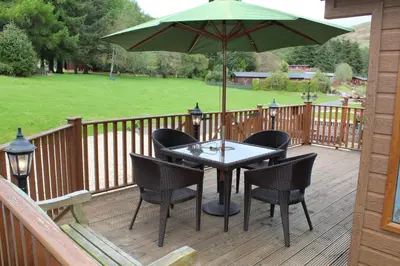 a table with chairs and an umbrella on a deck at Lazy Days Lodge, Glendevon, Perthshire in Glendevon