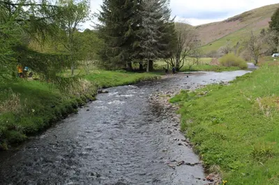 a river in the middle of a field with trees at Lazy Days Lodge, Glendevon, Perthshire in Glendevon