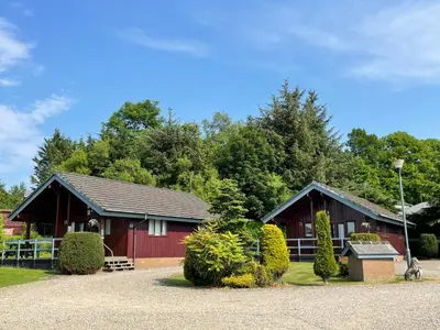 a red barn with a red fence and trees at Wellsfield Farm Holiday Lodges in Stirling