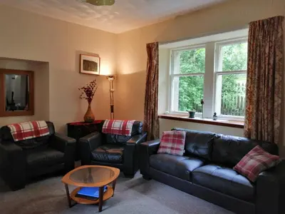 a living room with black leather furniture and a window at The Maid's House in Lanark
