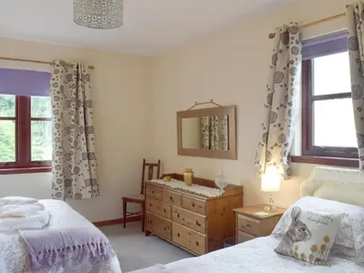 a bedroom with two beds and a dresser and a mirror at Cluniter Cottage in Innellan