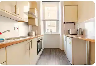 a kitchen with white cabinets and a wooden floor at 3 Bed Central Apartment - Pet Friendly & Parking in Edinburgh