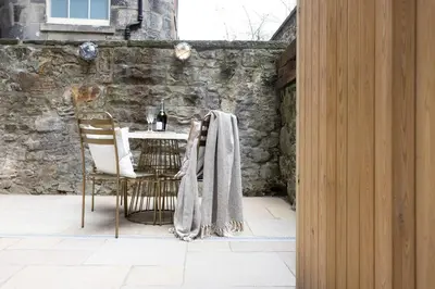 a table and chairs in a patio with a stone wall at 29 Queen Street Aparthotel in Edinburgh