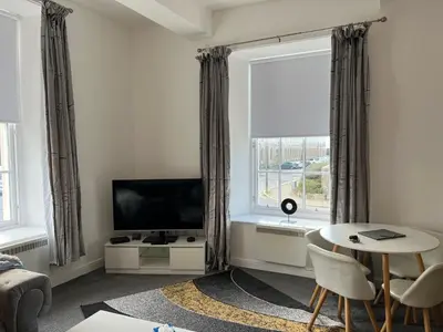 a living room with a television and a table and a window at Ayr Cozy Corner Apartment in Ayr