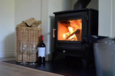 a bottle of wine and two wine glasses in front of a fireplace at Stable Cottage in Arrochar