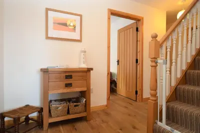a hallway with a staircase and a dresser and a stair case at High Beach Cottage in Kames