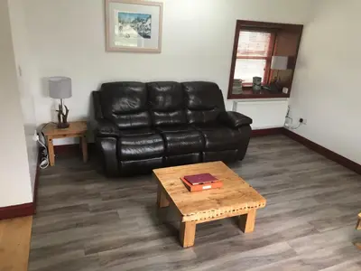 a living room with a black leather couch and a coffee table at Merrick Cottage in Bargrennan