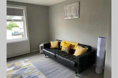 a living room with a black couch with yellow pillows at Beautiful two bedroom flat by the Loch in Balloch