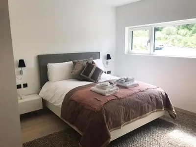 a white bedroom with a bed with a window at An Caisteal Lodge with cascading waterfall view in Crianlarich