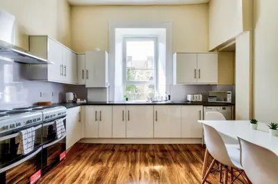 a kitchen with white cabinets and a table and a window at Stunning 5 bedroom apt, close to city centre, SEC, Hydro and motorway in Glasgow