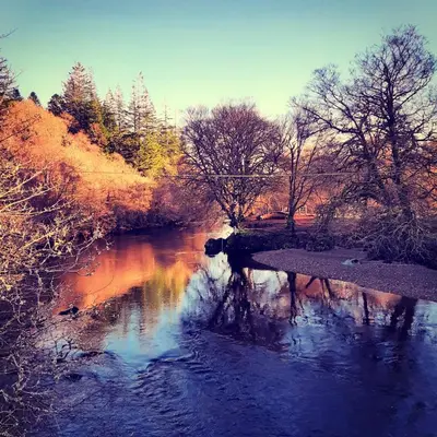 a river with a bridge and some trees and water at Glenorchy Lodge Hotel-Rooms Only in Dalmally