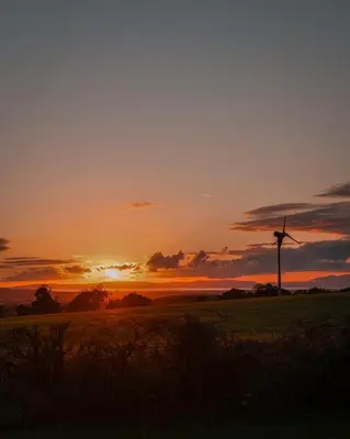 a sunset with a wind turbine in a field at Timber Valley Pods in Galston