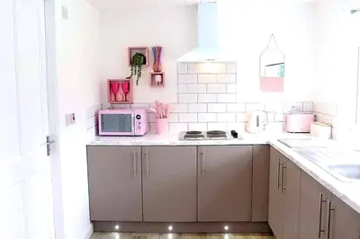 a white kitchen with a pink microwave on a counter at The Cabin with optional Hot Tub Projector DEPOSIT REQUIRED FOR PROJECTOR in Bonnybridge
