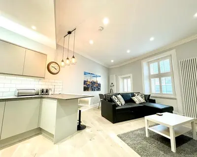 a living room with a black couch and a kitchen at Gorgeous 2BR & Central Edinburgh Bolt-hole in Edinburgh