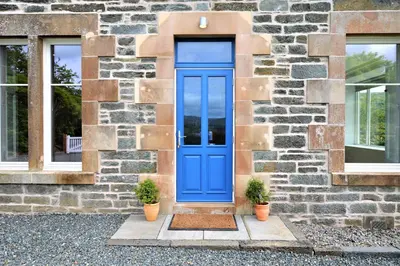 a blue door on a stone building with two potted plants at Greenlea in Strachur