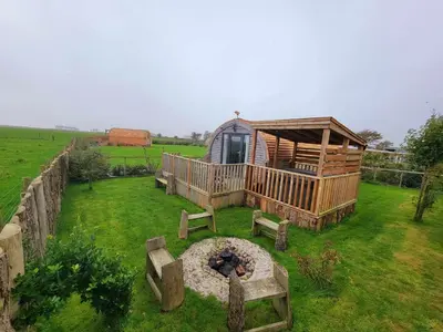 a cabin in the middle of a field with a fire pit at The Galloway Steading - The Stag Hoose family cabin with Hot Tub and Fire Pit in Glenluce