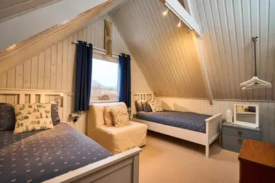 a bedroom with two beds and a chair and a window at The Moorings, overlooking Loch Fyne in Cairndow