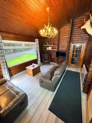 a living room with a couch and a chandelier at Antler Lodge Traditional Log Cabin in Dunoon