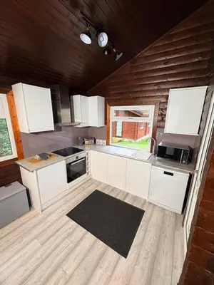 a kitchen with white cabinets and a wooden wall at Antler Lodge Traditional Log Cabin in Dunoon