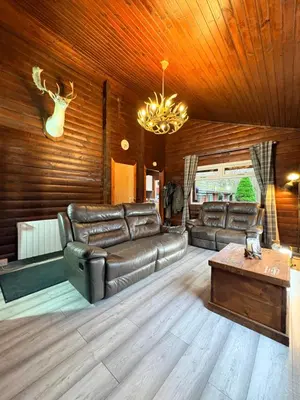 a living room with a leather couch and a table at Antler Lodge Traditional Log Cabin in Dunoon