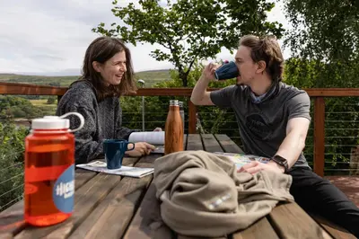 a woman sitting at a table drinking from a bottle at Highland Basecamp in Lochaline