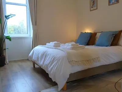 a bedroom with a bed with white sheets and blue pillows at Snug - Tearlag Apartment in Helensburgh