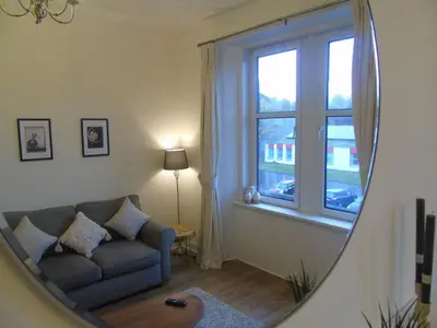 a mirror in a living room with a couch and a window at Snug - Tearlag Apartment in Helensburgh