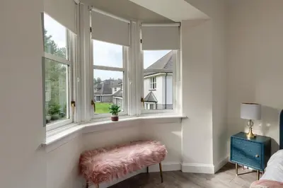 a bedroom with two windows and a pink ottoman at 3 bedroom Windsor Garden apartment by Gleneagles in Blackford