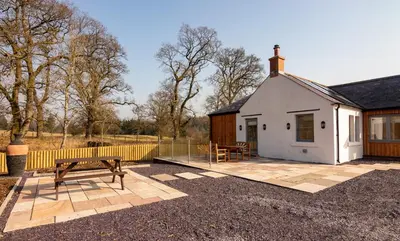 a white house with a picnic table and a bench at Slatehouse Cottage, Drumlanrig in Thornhill