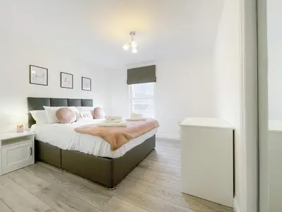 a white bedroom with a large bed with pink pillows at Pier View Apartment in Oban