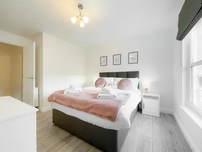a white bedroom with a large bed with pink pillows at Pier View Apartment in Oban