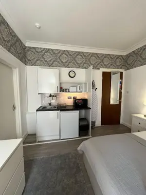 a bedroom with a bed and a kitchen with white cabinets at Bemersyde Guest House in Mansewood